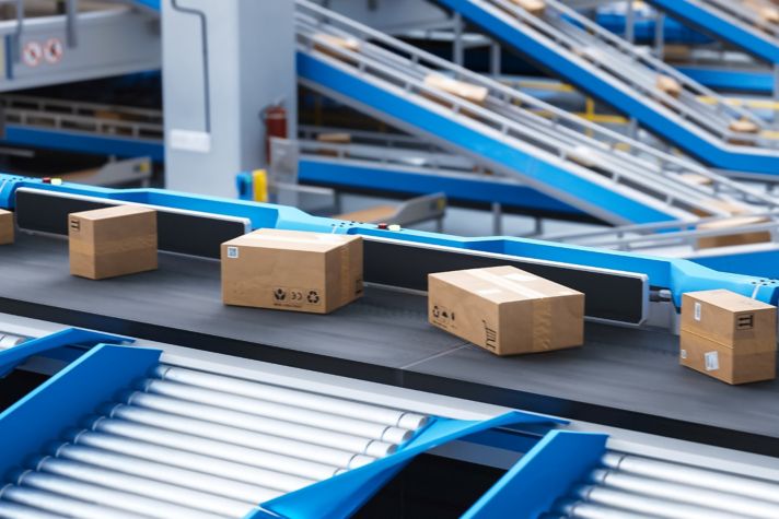An indoor warehouse features a conveyor belt system with cardboard boxes being sorted, highlighting the efficiency of modern logistics and supply chain management.