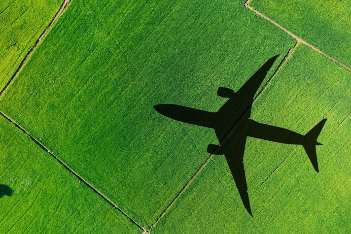 An aerial view captures the shadow of an airplane flying over vibrant green fields, highlighting the contrast between nature and flight.