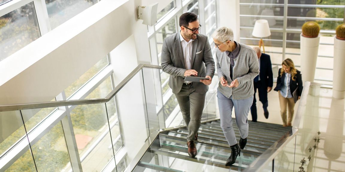 Professionals engaging in conversation while walking up a bright, glass-walled staircase in a contemporary office.