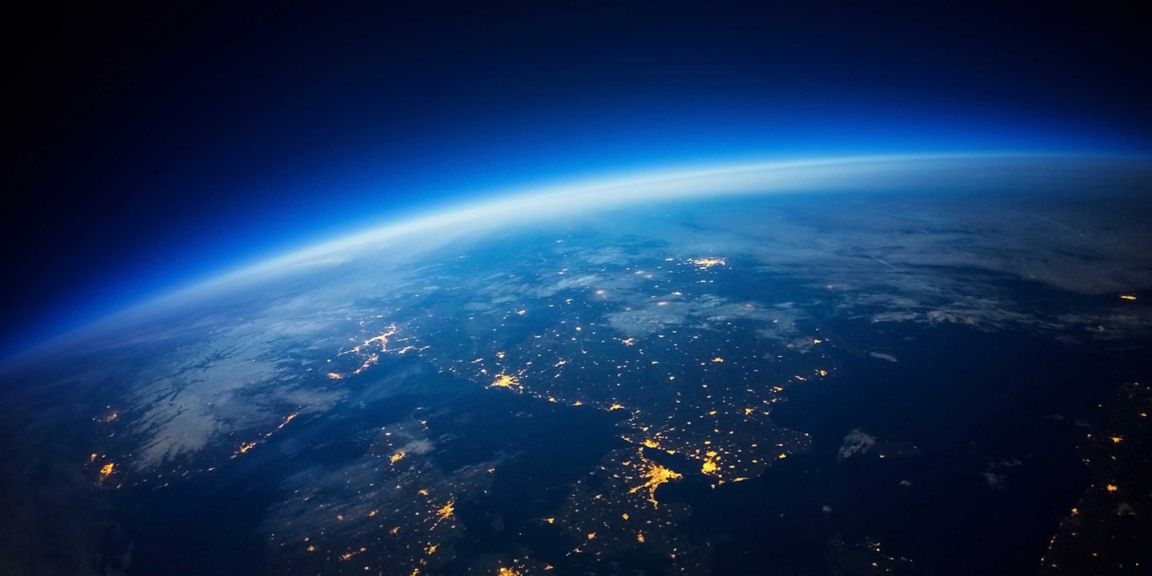 A stunning view of Earth’s curvature from space, showing illuminated city lights and a glowing blue atmosphere fading into the darkness of space.