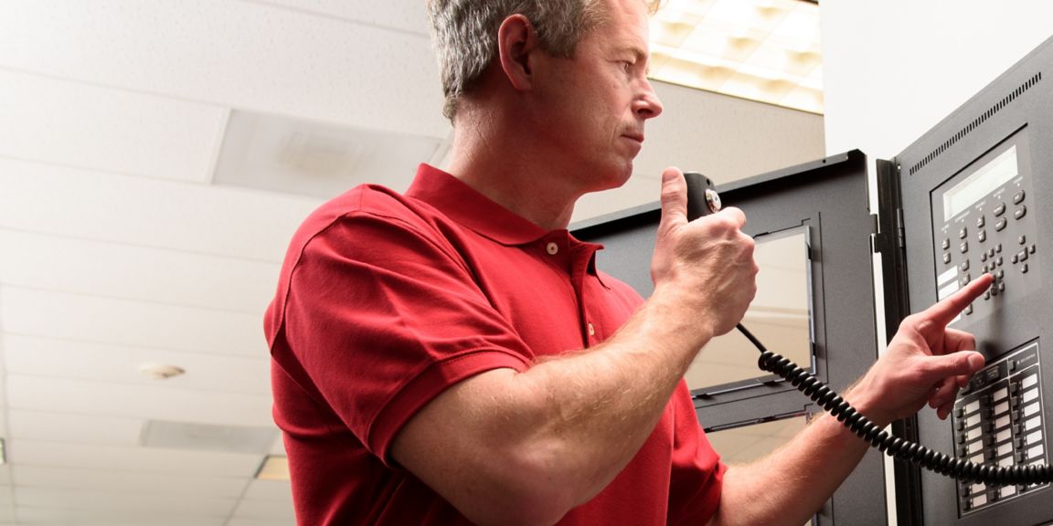 An individual in a red polo shirt operates a security control panel, emphasizing the importance of effective communication in building safety management. 