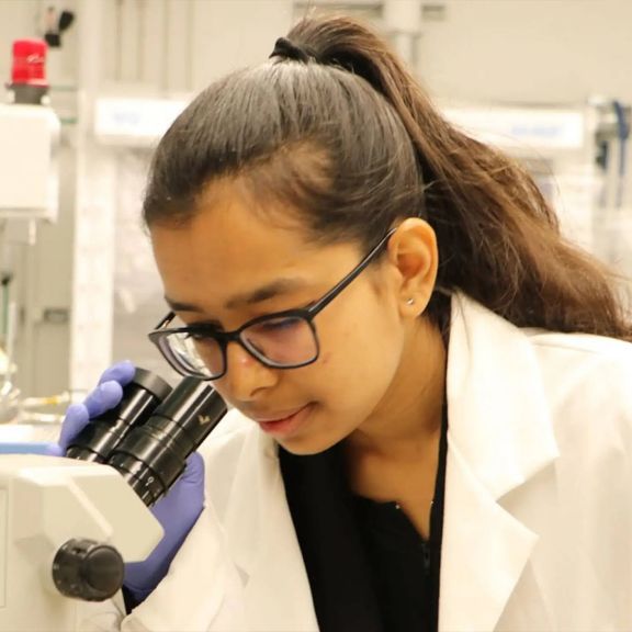 A researcher examines samples through a microscope, representing the vital role of women in scientific advancements.