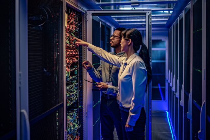 Male and female IT engineers checking servers in server room with help of tablet.