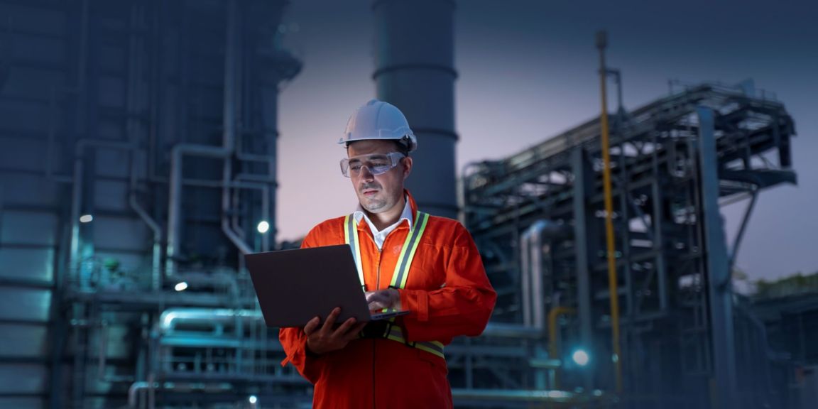 Engineer with laptop in front of industrial setting at night