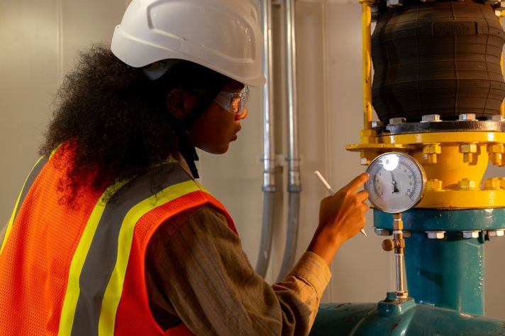 A worker in a safety vest checks a pressure gauge on a large valve in an industrial setting, ensuring operational efficiency and safety.