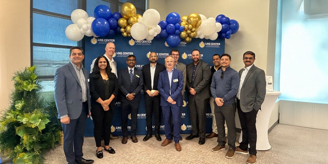 Group photo from an LNG Center of Excellence event featuring industry professionals gathered in front of branded backdrop and decorative balloons, highlighting collaboration, networking, and innovation in the liquefied natural gas sector.