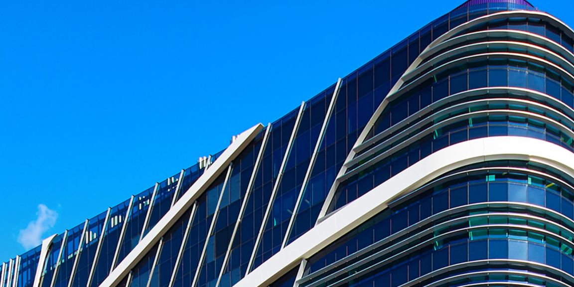 Discover the stunning design of a contemporary building with sleek lines, glass facades, and unique geometric patterns set against a vibrant blue sky.