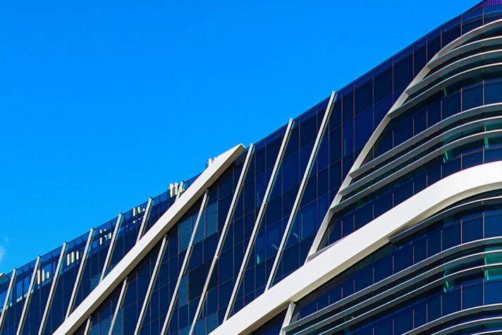 Discover the stunning design of a contemporary building with sleek lines, glass facades, and unique geometric patterns set against a vibrant blue sky.