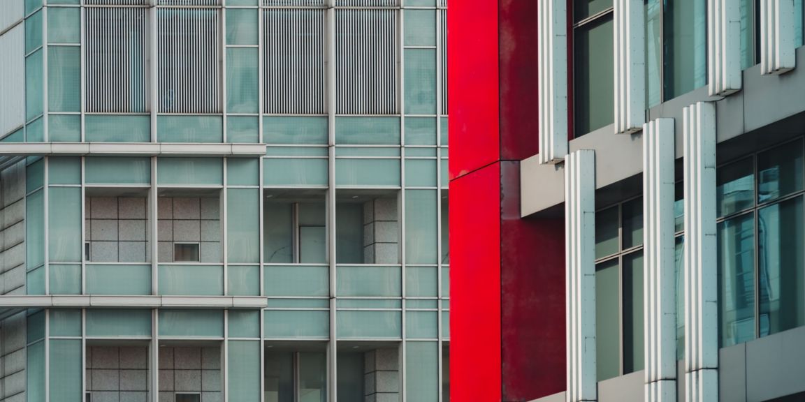 Close-up view of two modern city buildings/windows in grey, with a red accent pillar.