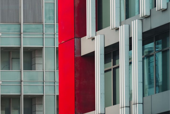 Close-up view of two modern city buildings/windows in grey, with a red accent pillar.