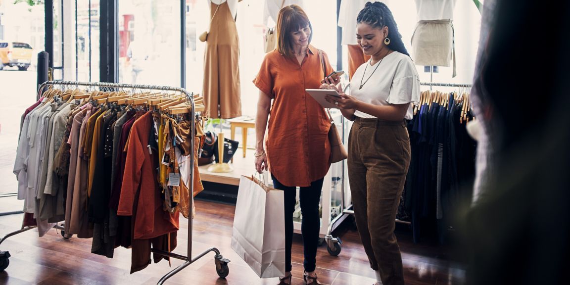 Shop assistant using a digital tablet while assisting a customer in a boutique