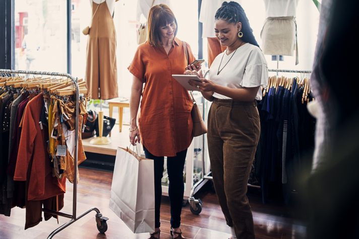 shop assistant using a digital tablet while assisting a customer in a boutique