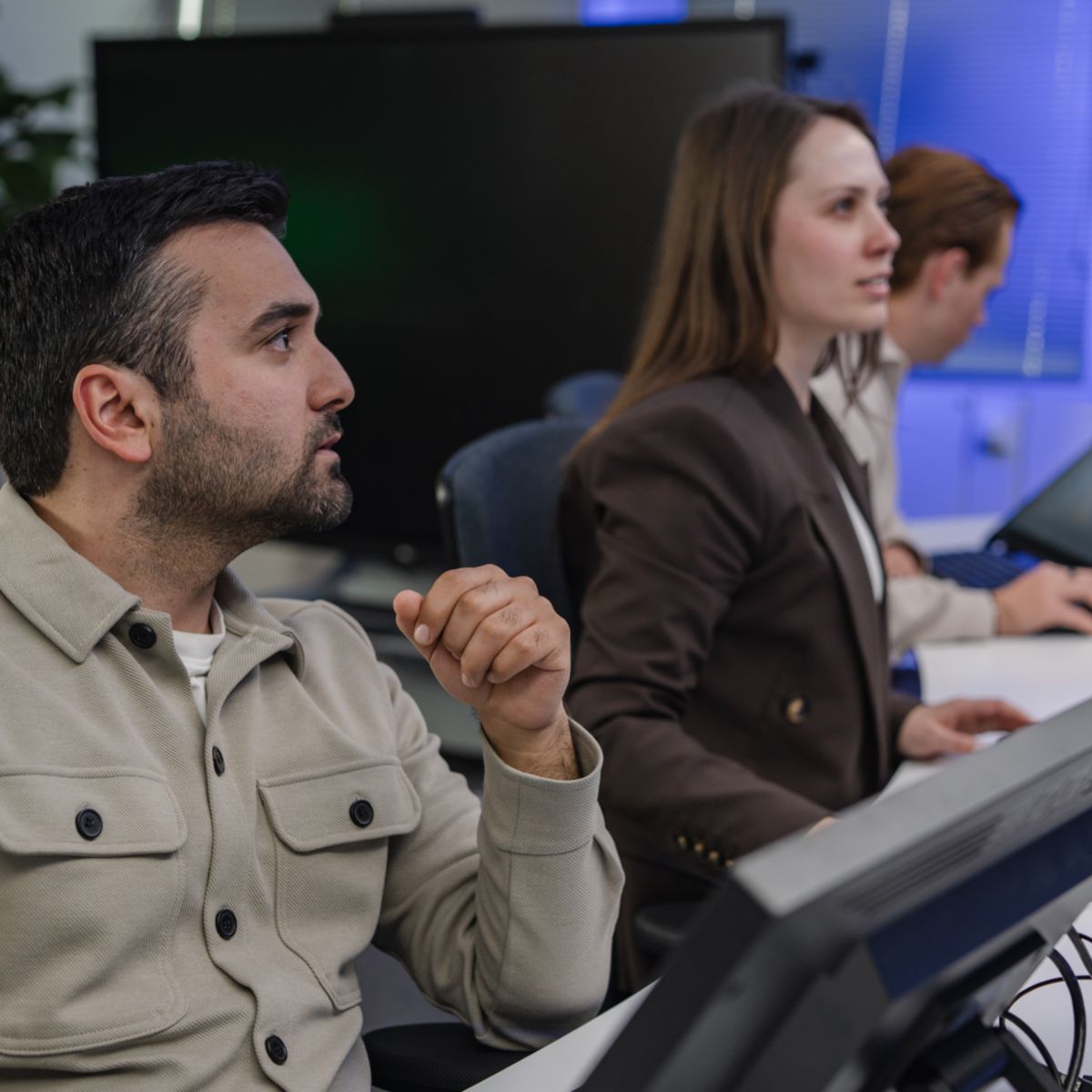 Side view of a team collaborating at monitoring stations, analyzing data and coordinating operations in a control room setting.
