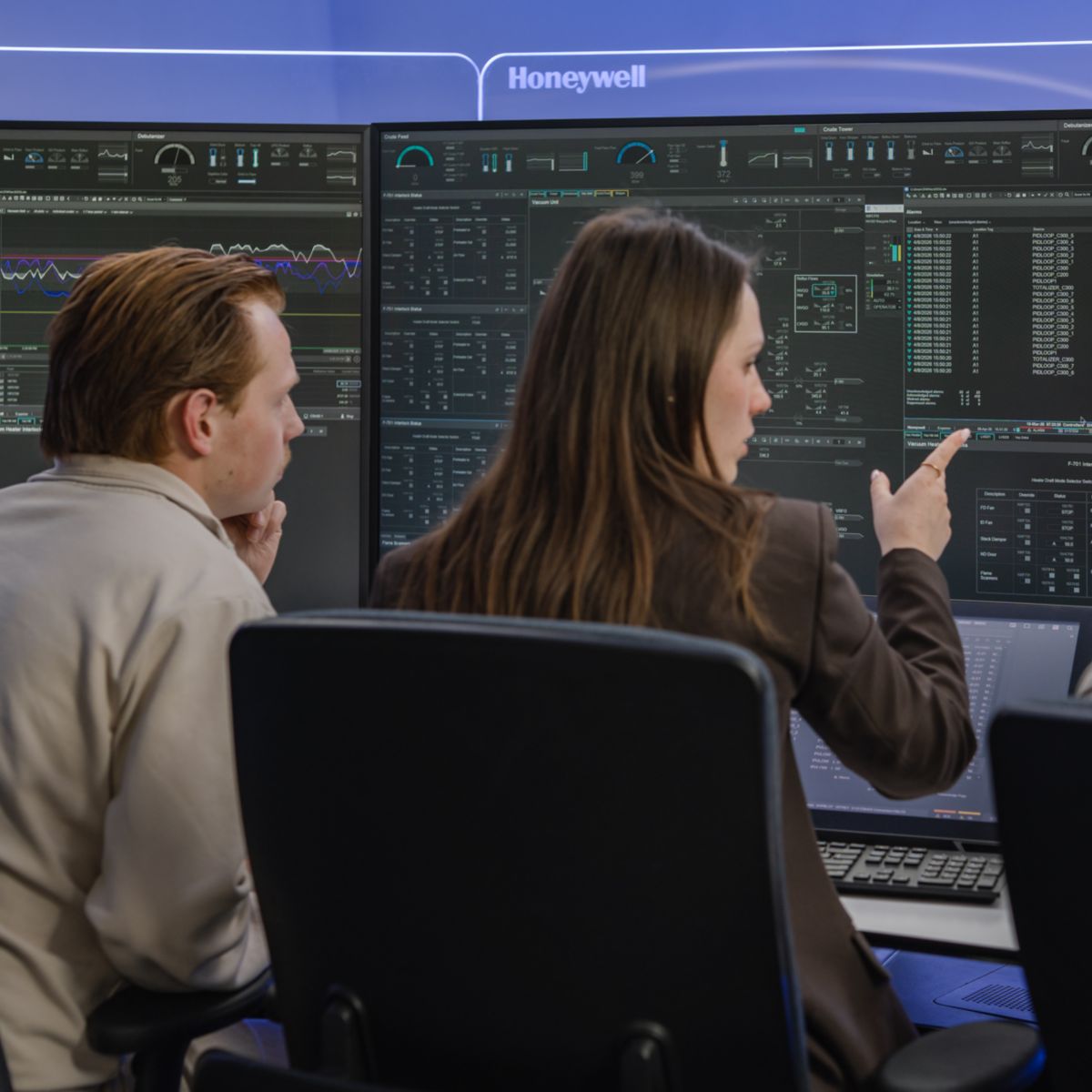 Back view of a team monitoring large display screens in an operations center, focusing on data analysis and system performance.
