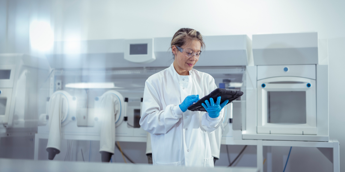 Research professional holding a laptop while monitoring equipment.