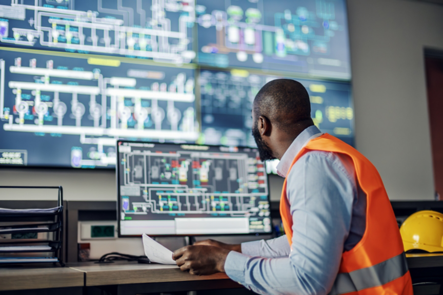 African american engineer operating a supervisory control and data acquisition system, checking schematics and process flow on multiple screens in a modern control room