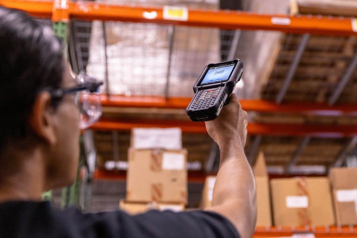 A warehouse worker uses a handheld barcode scanner to manage inventory efficiently in a busy storage environment. Perfect for enhancing supply chain operations.