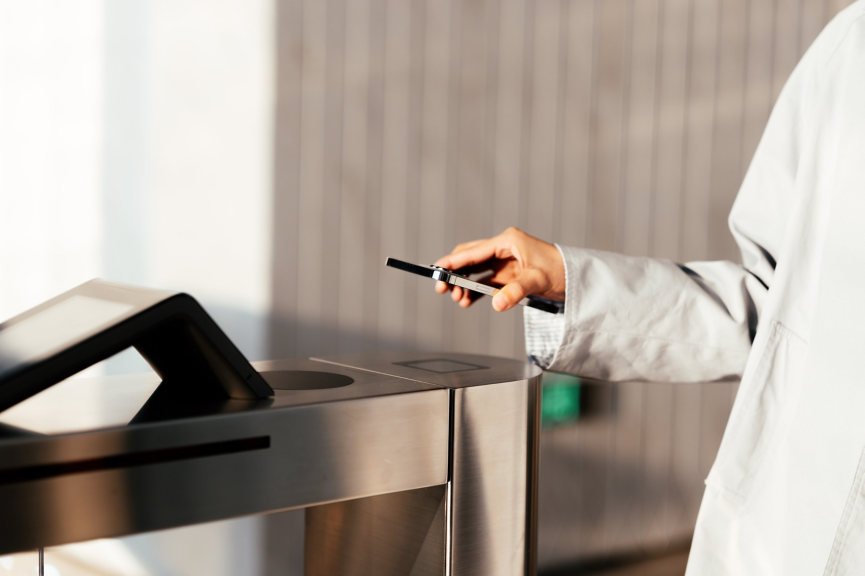 An employee uses their smartphone to scan through a modern electronic security turnstile at an office building entrance.
