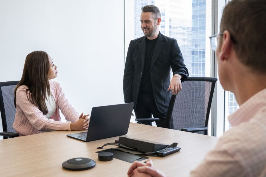 A male manager presents ideas to colleagues during a collaborative business strategy meeting in a modern, light-filled office boardroom.