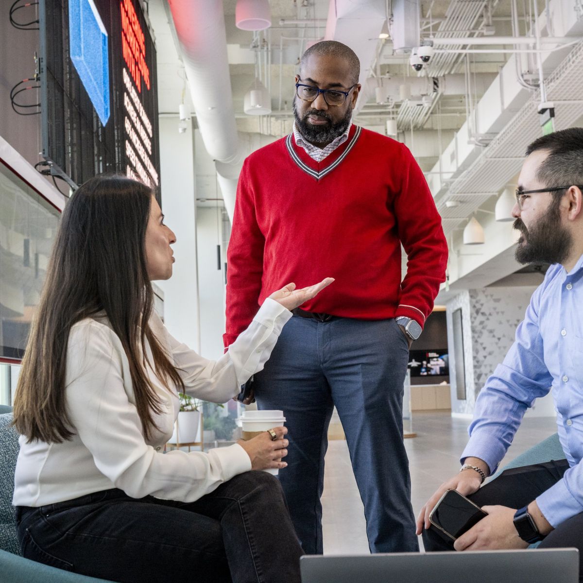 A diverse group of three professionals engages in a collaborative discussion within a modern, open-concept office workspace.
