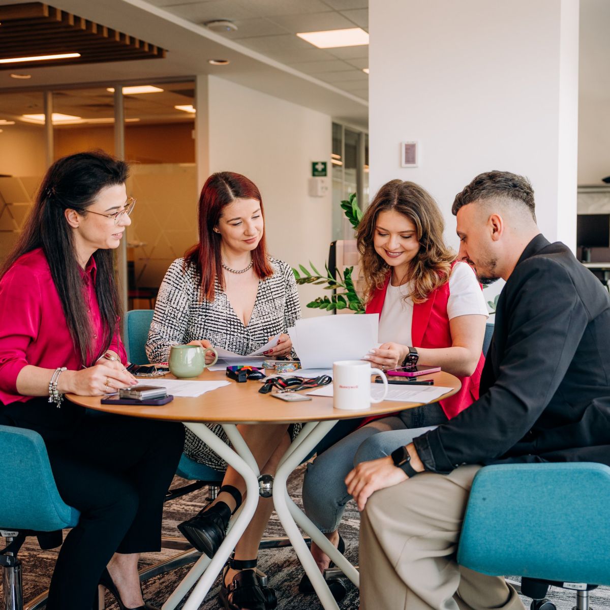 A diverse group of professionals collaborates around a table in a modern office space, reviewing documents and discussing business initiatives together.