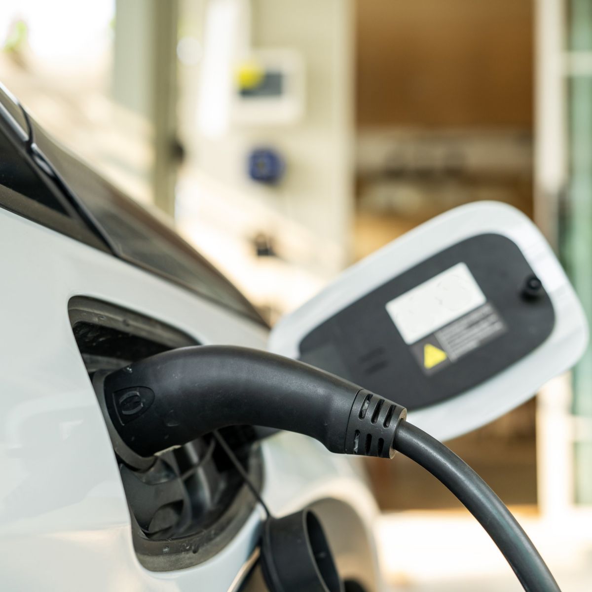 Close-up of a power cable connected to a white electric car at a home charging station.