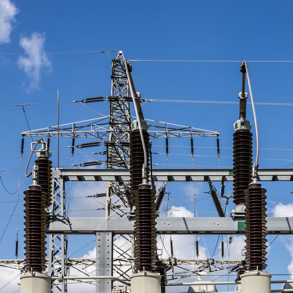 High-voltage ceramic insulators and transmission infrastructure stand against a clear blue sky in this industrial power grid installation.