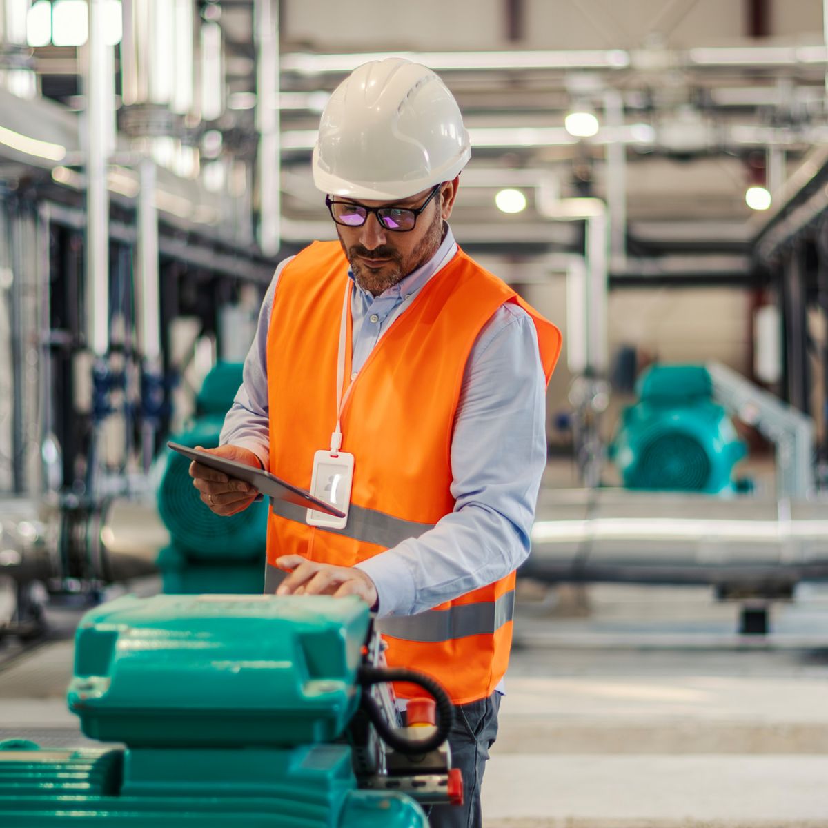 Engineer inspecting industrial pumping equipment using a tablet, representing fluid handling systems, plant reliability, and process optimisation in industrial operations.