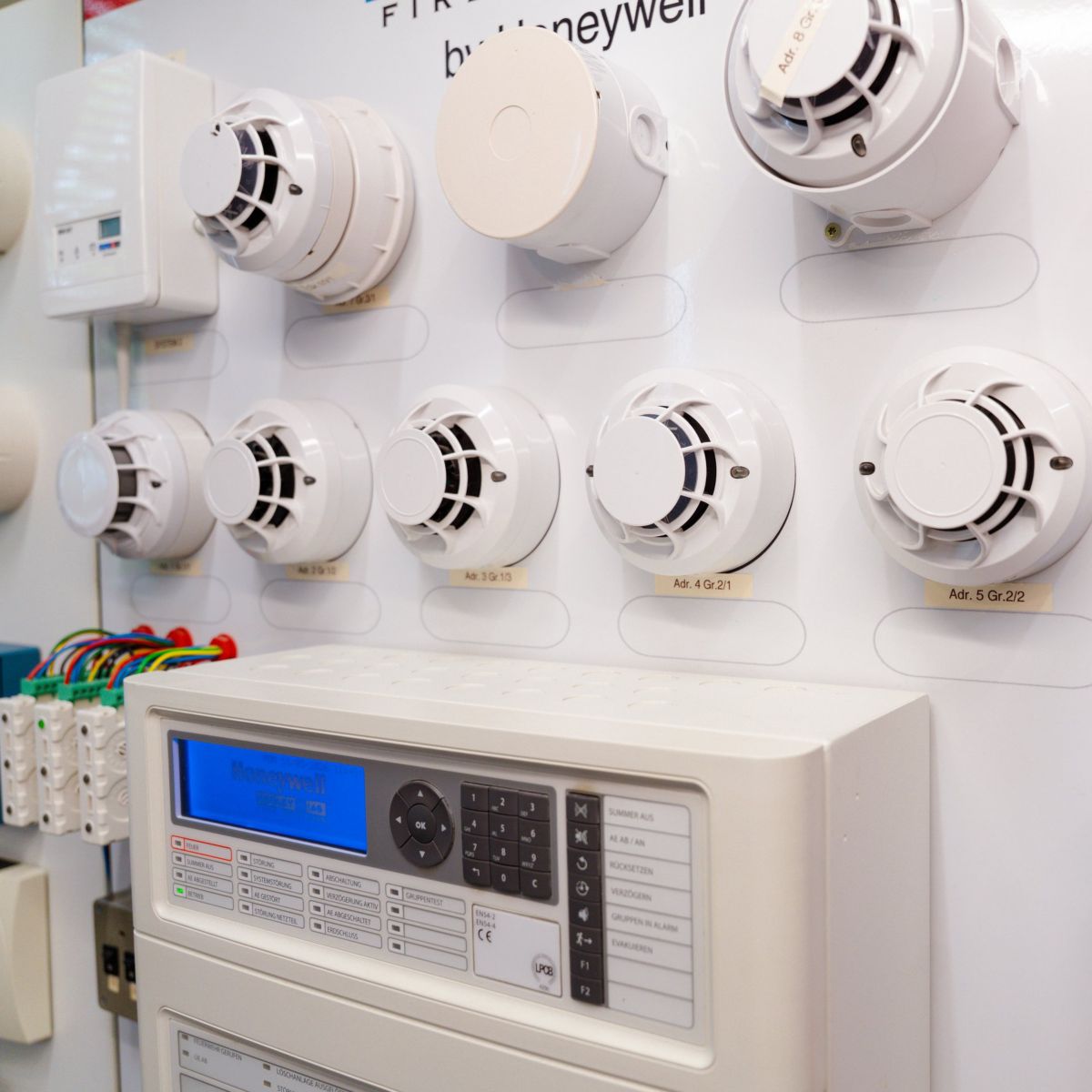 A technical display panel showcases various Honeywell smoke detectors and control components for industrial fire safety and monitoring applications.