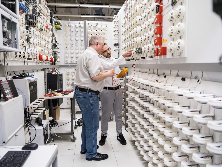 Engineers testing and configuring smoke detectors in a fire safety lab environment.
