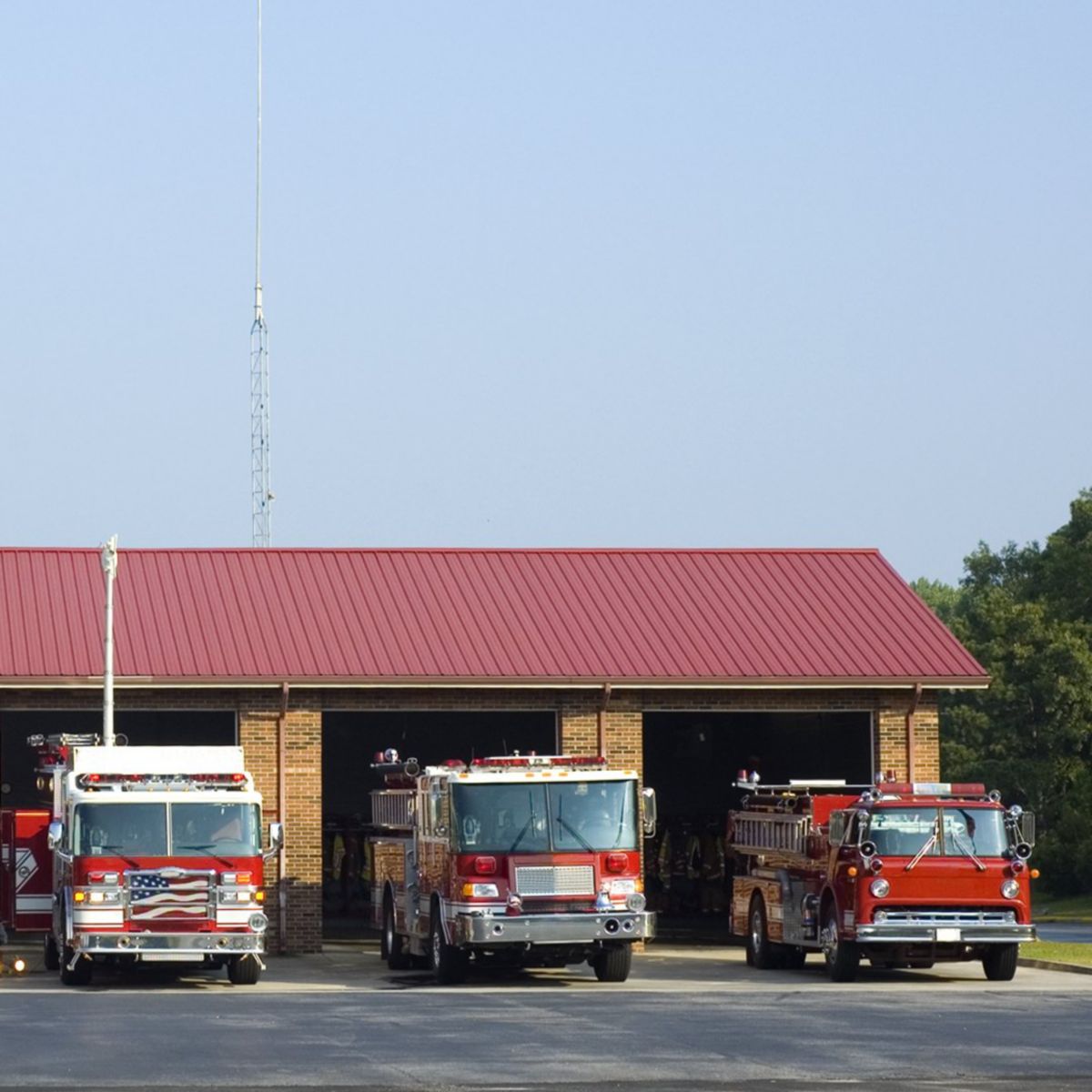Four red fire engines parked in front of a brick fire station building under a clear blue sky.