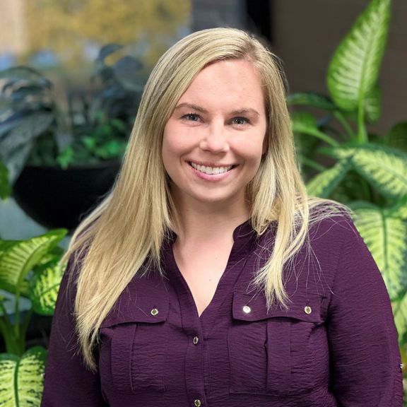 Professional portrait of Megan Kubacki, captured in a clean studio setting with plants as a background.