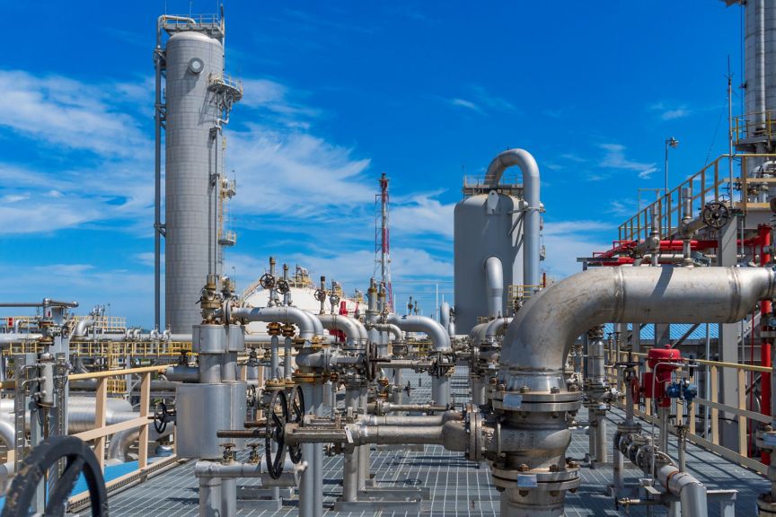 A panoramic view of an industrial gas processing facility featuring complex piping and storage tanks against a bright blue sky.