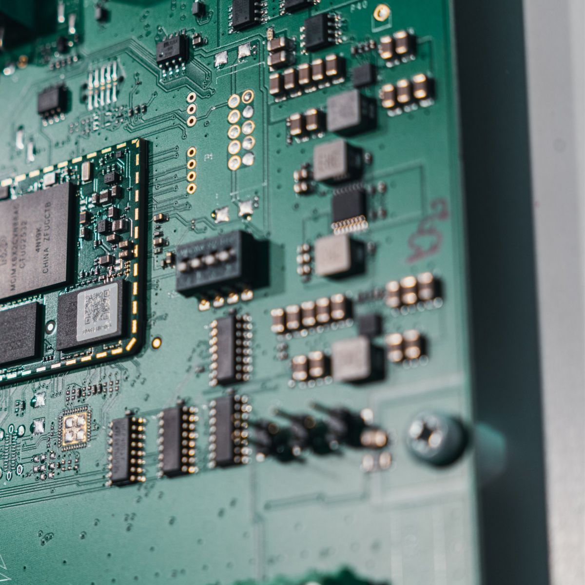 Close-up macro shot of a complex green circuit board featuring various integrated chips and surface-mount electronic components.