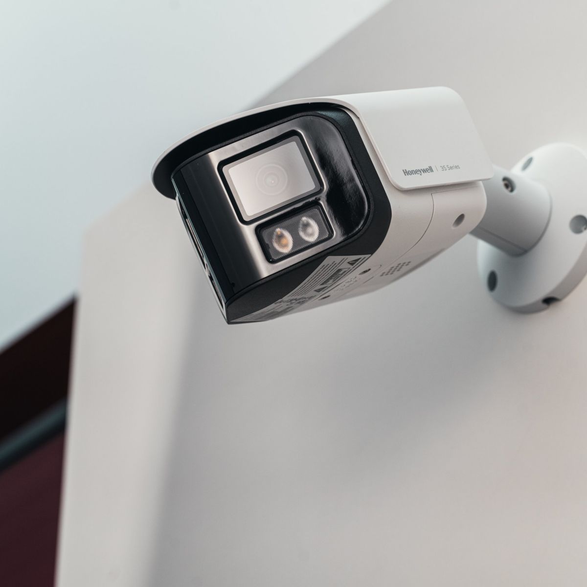 A low-angle shot of a Honeywell 35 Series surveillance camera mounted on a plain white wall for industrial security monitoring.