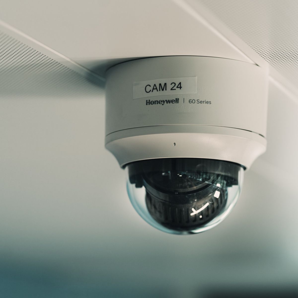 A low-angle close-up of a Honeywell 60 Series dome security camera mounted on a textured white ceiling.