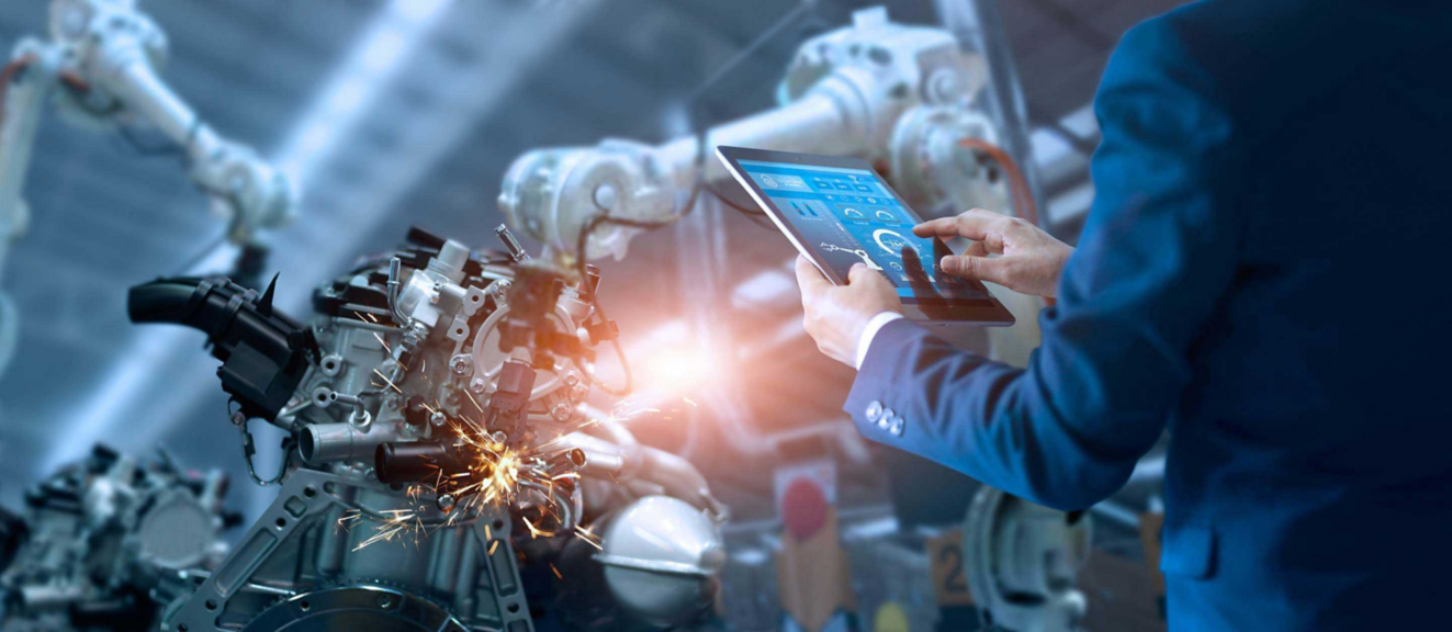 A professional uses a tablet to monitor and control robotic machinery in a modern manufacturing environment.