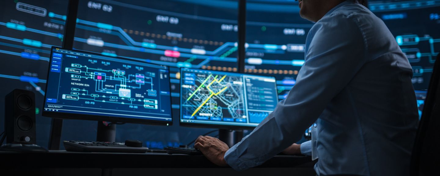 Professional IT Technical Support Specialist and Software Developer Working on Computer in Monitoring Control Room with Digital Screens. Employee Uses Headphones with Mic and Talking on a Call.