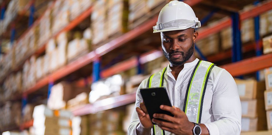 A warehouse professional uses a tablet to manage inventory in a logistics environment—highlighting the integration of Honeywell's Momentum WES mobile technology in modern supply chain and manufacturing operations.