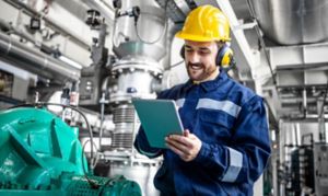 Industrial engineer standing by gas generator in power plant and controlling electricity production on his tablet.