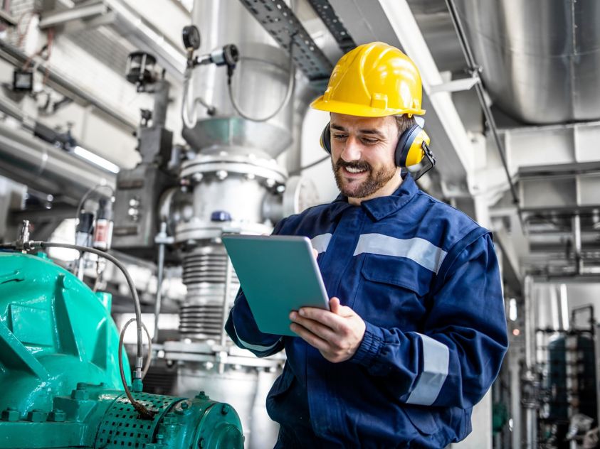 Industrial engineer standing by gas generator in power plant and controlling electricity production on his tablet.
