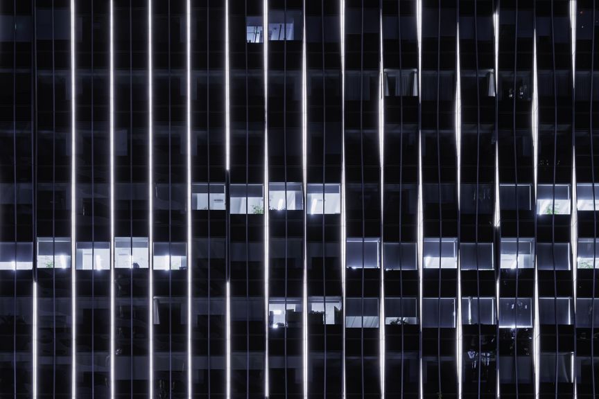 Vertical light strips emphasize the architectural grid of a modern high-rise office building during the night.