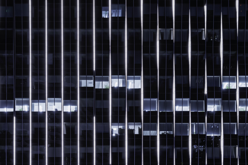Vertical light strips emphasize the architectural grid of a modern high-rise office building during the night.