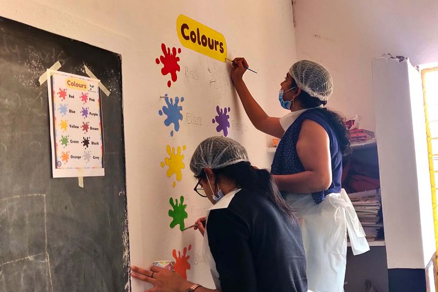 Volunteers teach children about colors by painting a colorful mural in a classroom setting.