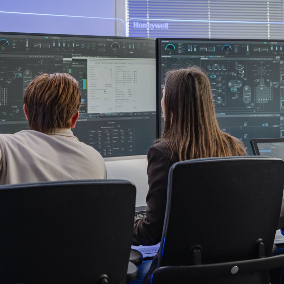 Three professionals analyze complex data and industrial workflows on large-scale digital displays in a modern Honeywell control room.
