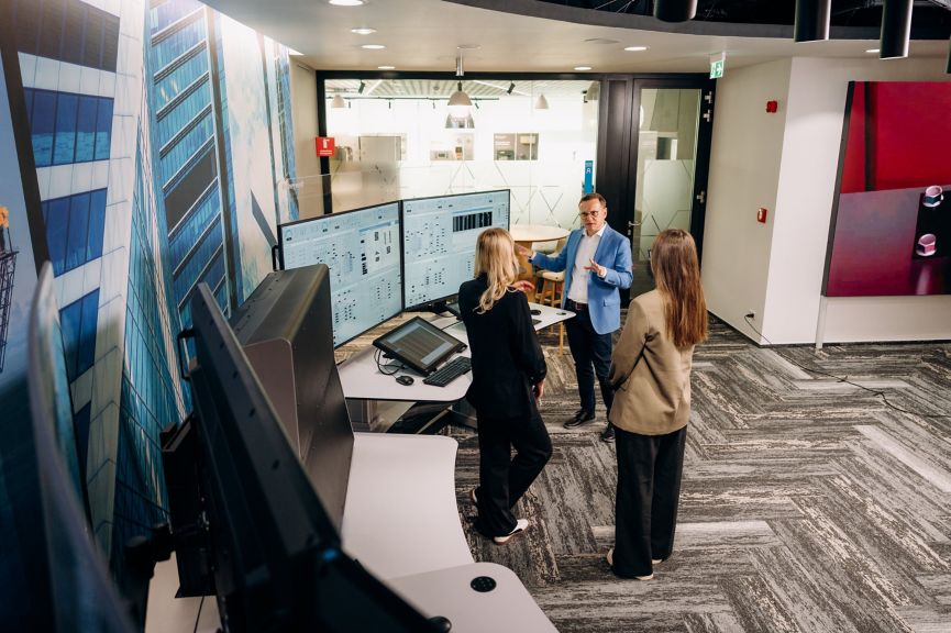 Professional team members discuss technical data on multiple monitors within a modern corporate industrial control facility.