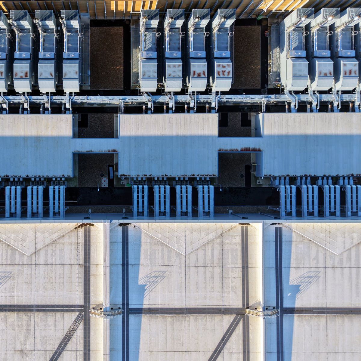 An overhead aerial view of an industrial facility roof featuring modular HVAC cooling units and large structural concrete ventilation segments.