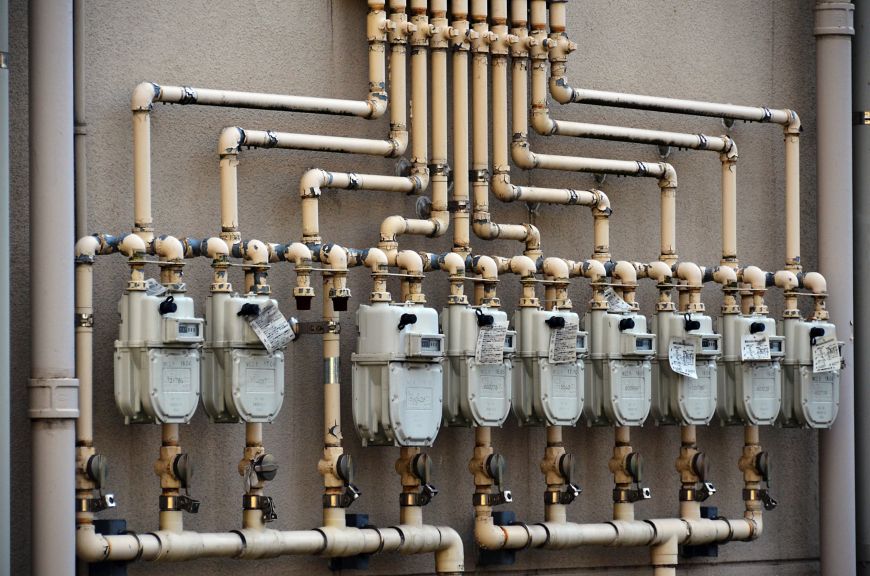 A series of industrial gas meters with interconnected piping mounted on an exterior wall.