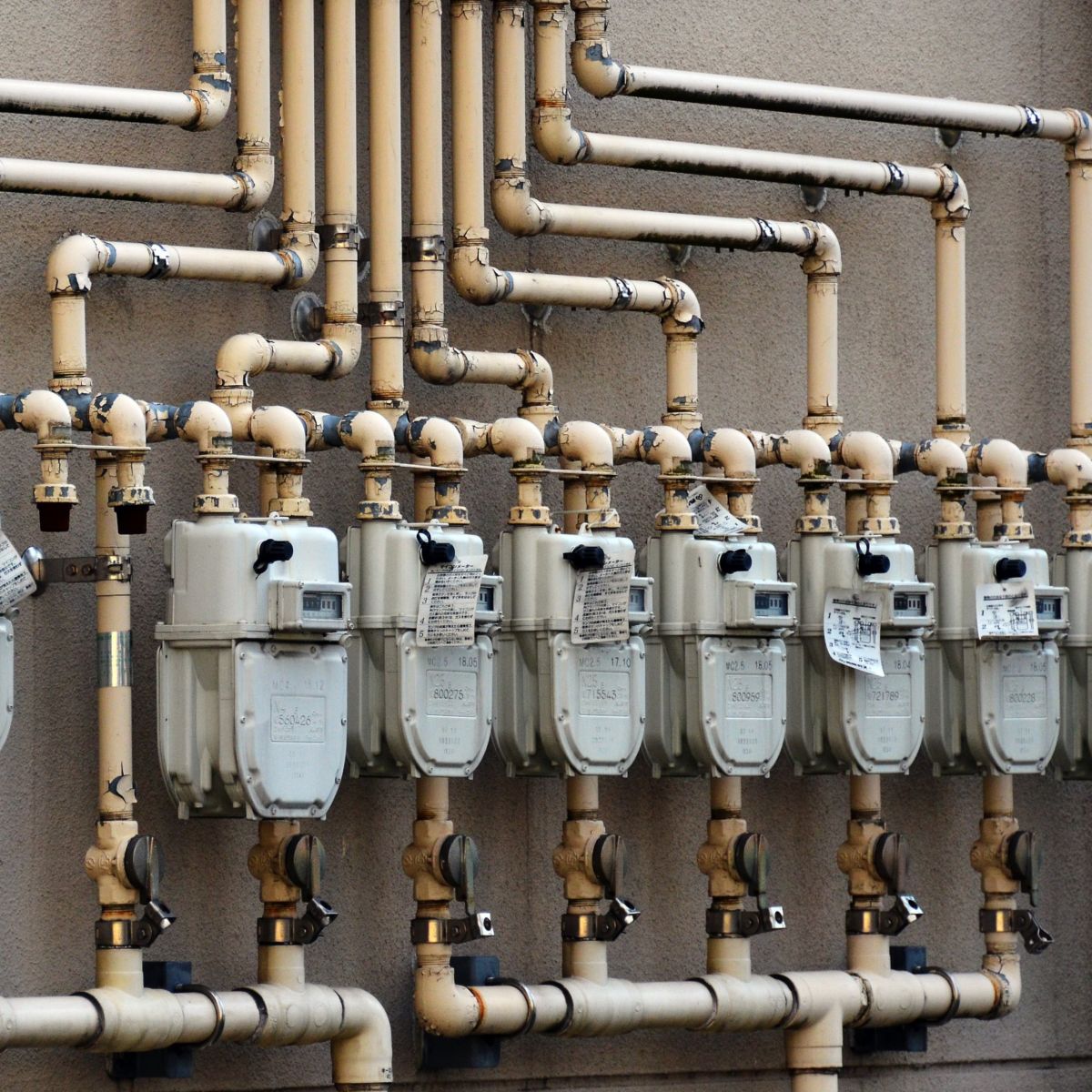 A series of industrial gas meters with interconnected piping mounted on an exterior wall.