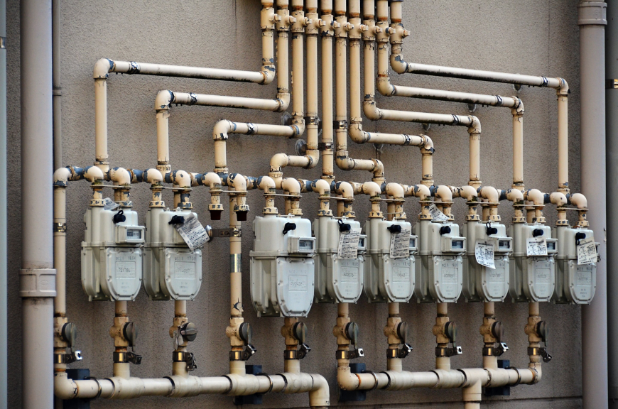 A series of industrial gas meters with interconnected piping mounted on an exterior wall.
